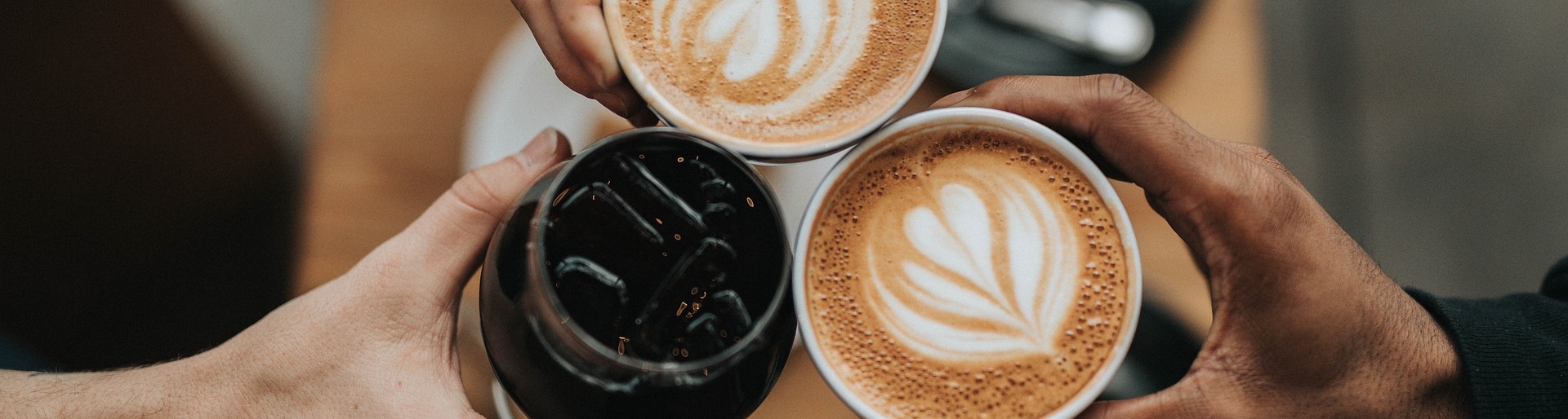 Ein Café in Baden - Nahaufnahme von drei Personen, die mit zwei Kaffees und einem Glas Cola anstoßen