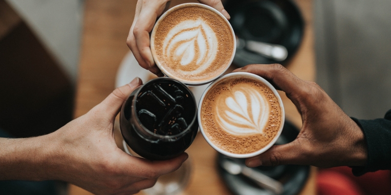Ein Café in Baden - Nahaufnahme von drei Personen, die mit zwei Kaffees und einem Glas Cola anstoßen
