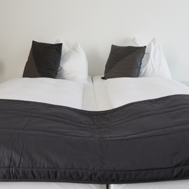 Zimmer nahe Zürich mit Doppelbett, weißer und grauer Bettwäsche und zwei schlanken Nachttischleuchten