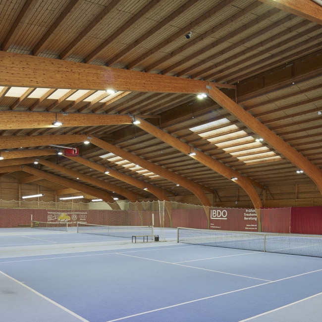 Große Tennishalle mit drei Spielfeldern und einer Decke aus Holz