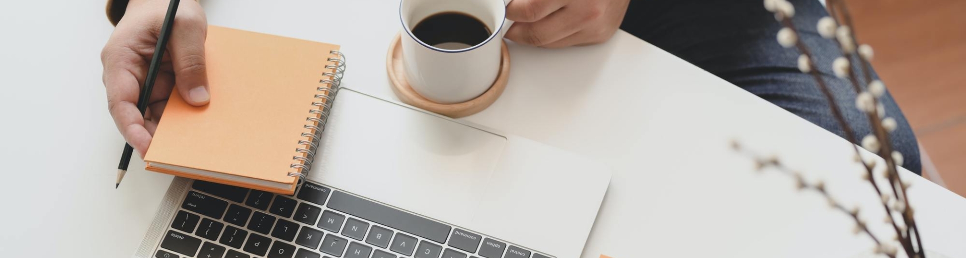 Blick auf einen Schreibtisch mit Laptop, Kaffeetasse und Notizbuch 