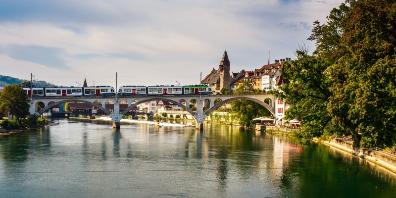 Ausflugsziele im Aargau - Blick auf eine Stadt im Aargau mit einem Fluss, der hindurchfließt, und einer Straßenbahn, die auf der Brücke über dem Fluss fährt
