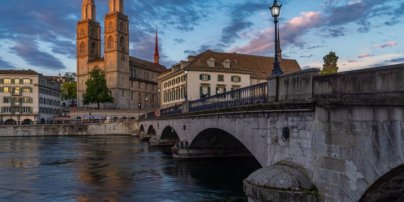 Tagesausflug nach Zürich - malerische Szene in Zürich mit einer historischen Steinbrücke im Vordergrund, die über einen ruhigen Fluss führt