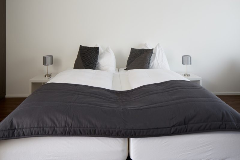 Zimmer nahe Zürich mit Doppelbett, weißer und grauer Bettwäsche und zwei schlanken Nachttischleuchten
