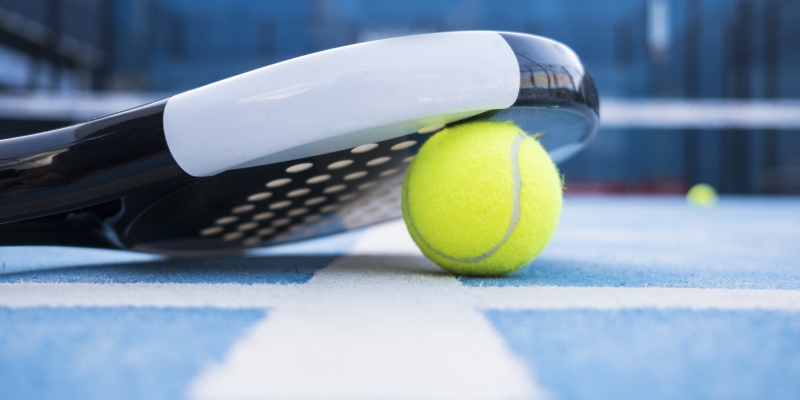 Close-up of a padel racket resting on a yellow tennis ball in a sports hotel in Switzerland